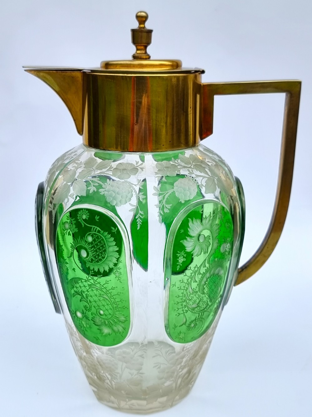 A clear glass claret jug featuring green overlay panels etched with floral motifs, topped with a metal collar, spout, lid, and geometric handle. View XVI