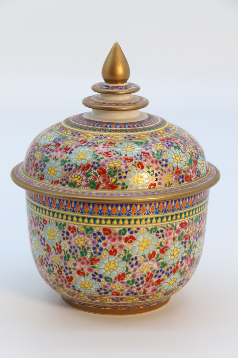 A polychrome enamelled ceramic jar with a fitted stepped lid featuring intricate floral motifs and a gilded conical finial.