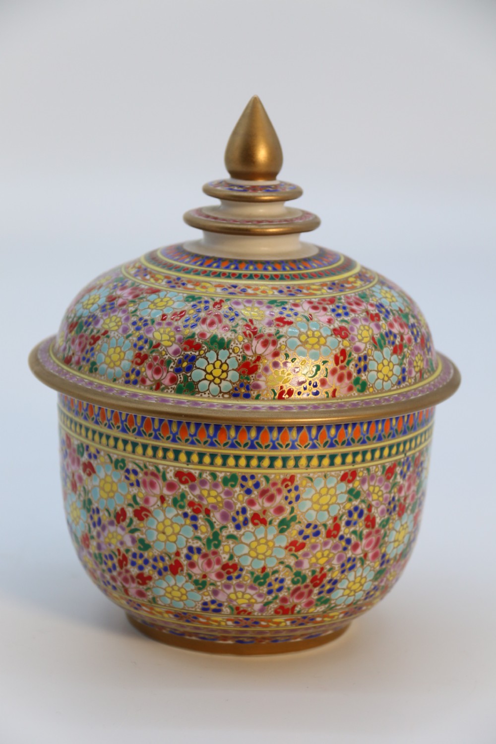 A polychrome enamelled ceramic jar with a fitted stepped lid featuring intricate floral motifs and a gilded conical finial. View II