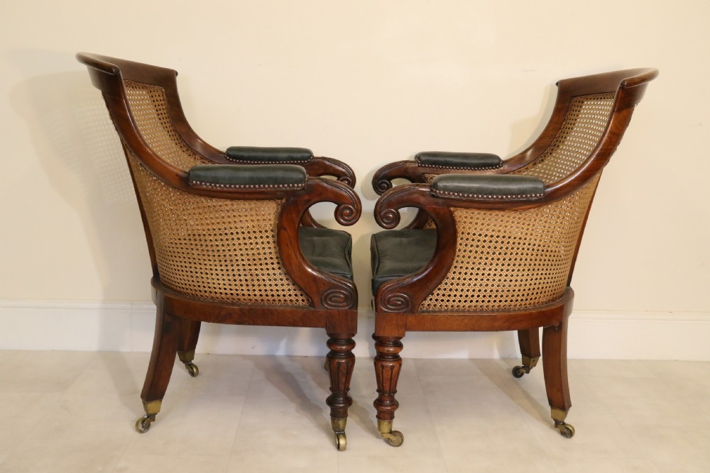 A pair of Regency rosewood bergere library armchairs with hand-woven cane panels, deep green leather cushions, scrolled arms, and turned legs on brass castors. View II