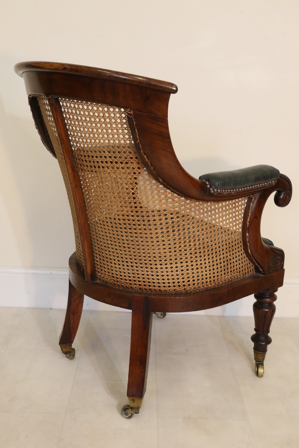 A pair of Regency rosewood bergere library armchairs with hand-woven cane panels, deep green leather cushions, scrolled arms, and turned legs on brass castors. View VII