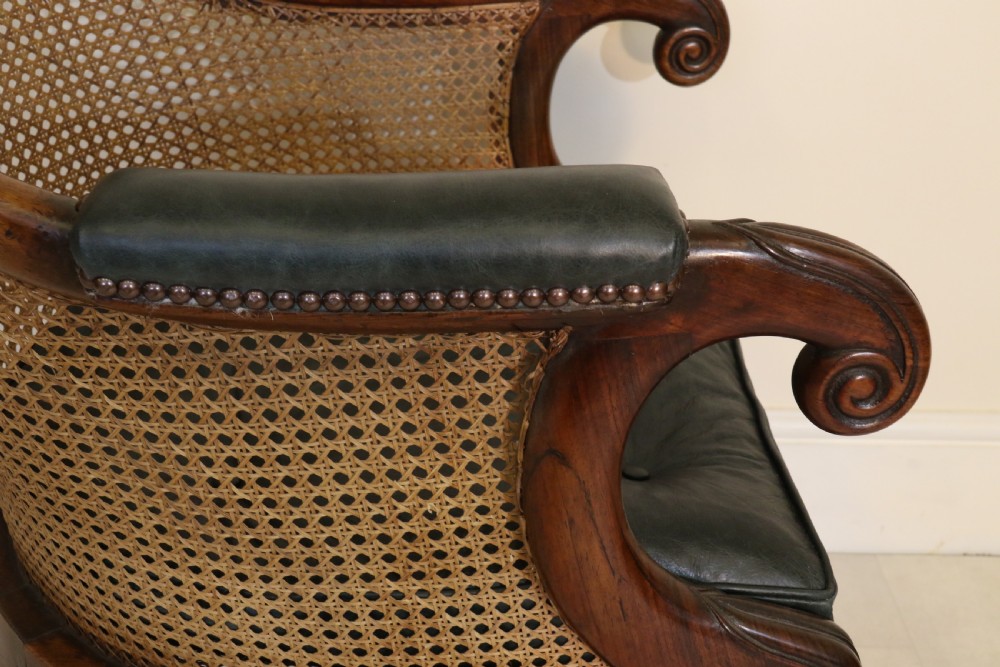 A pair of Regency rosewood bergere library armchairs with hand-woven cane panels, deep green leather cushions, scrolled arms, and turned legs on brass castors. View VIII
