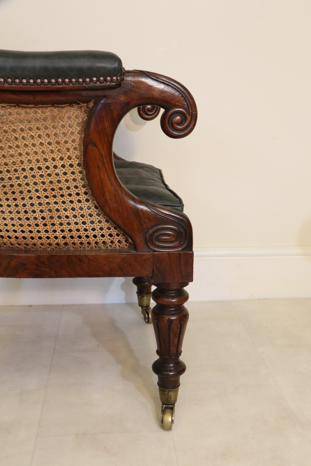 A pair of Regency rosewood bergere library armchairs with hand-woven cane panels, deep green leather cushions, scrolled arms, and turned legs on brass castors. View IX