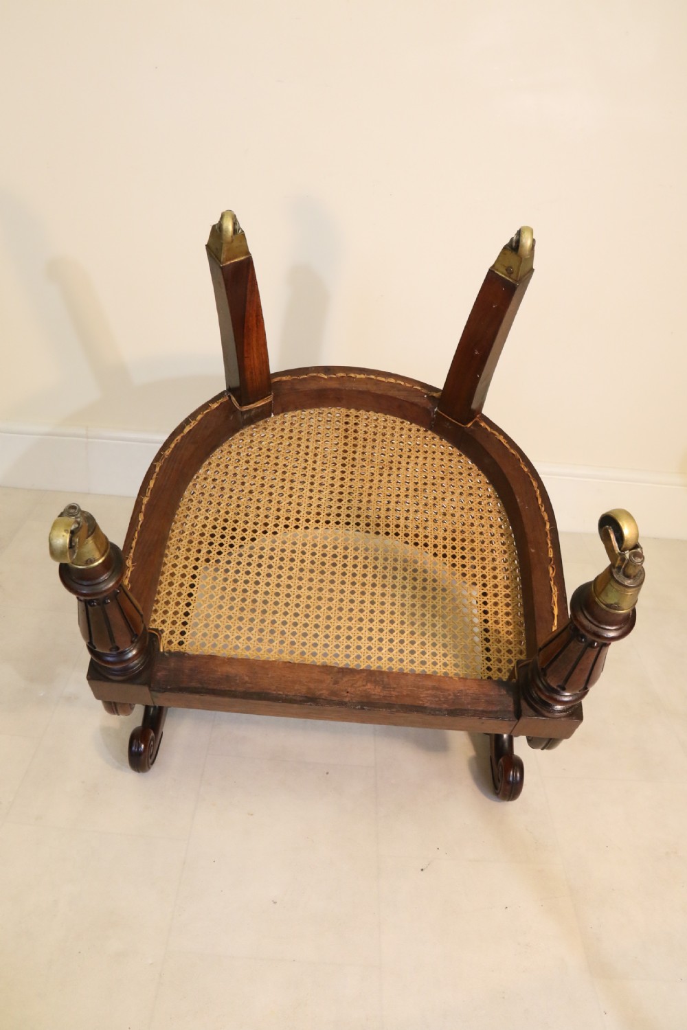 A pair of Regency rosewood bergere library armchairs with hand-woven cane panels, deep green leather cushions, scrolled arms, and turned legs on brass castors. View X