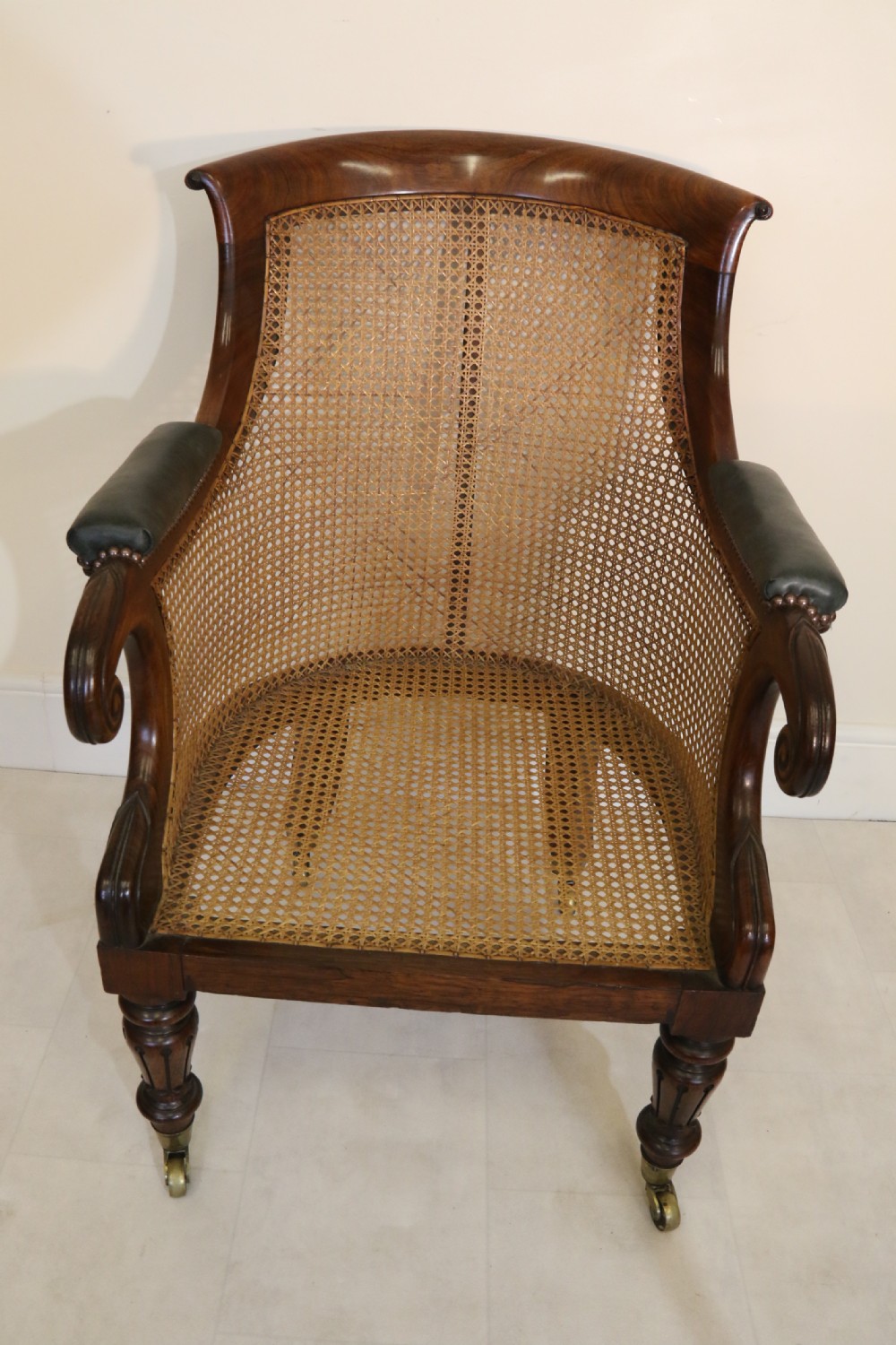 A pair of Regency rosewood bergere library armchairs with hand-woven cane panels, deep green leather cushions, scrolled arms, and turned legs on brass castors. View XI