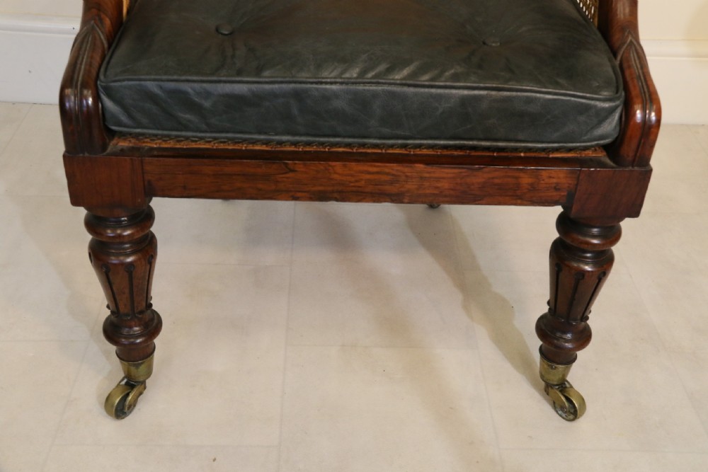 A pair of Regency rosewood bergere library armchairs with hand-woven cane panels, deep green leather cushions, scrolled arms, and turned legs on brass castors. View XIII