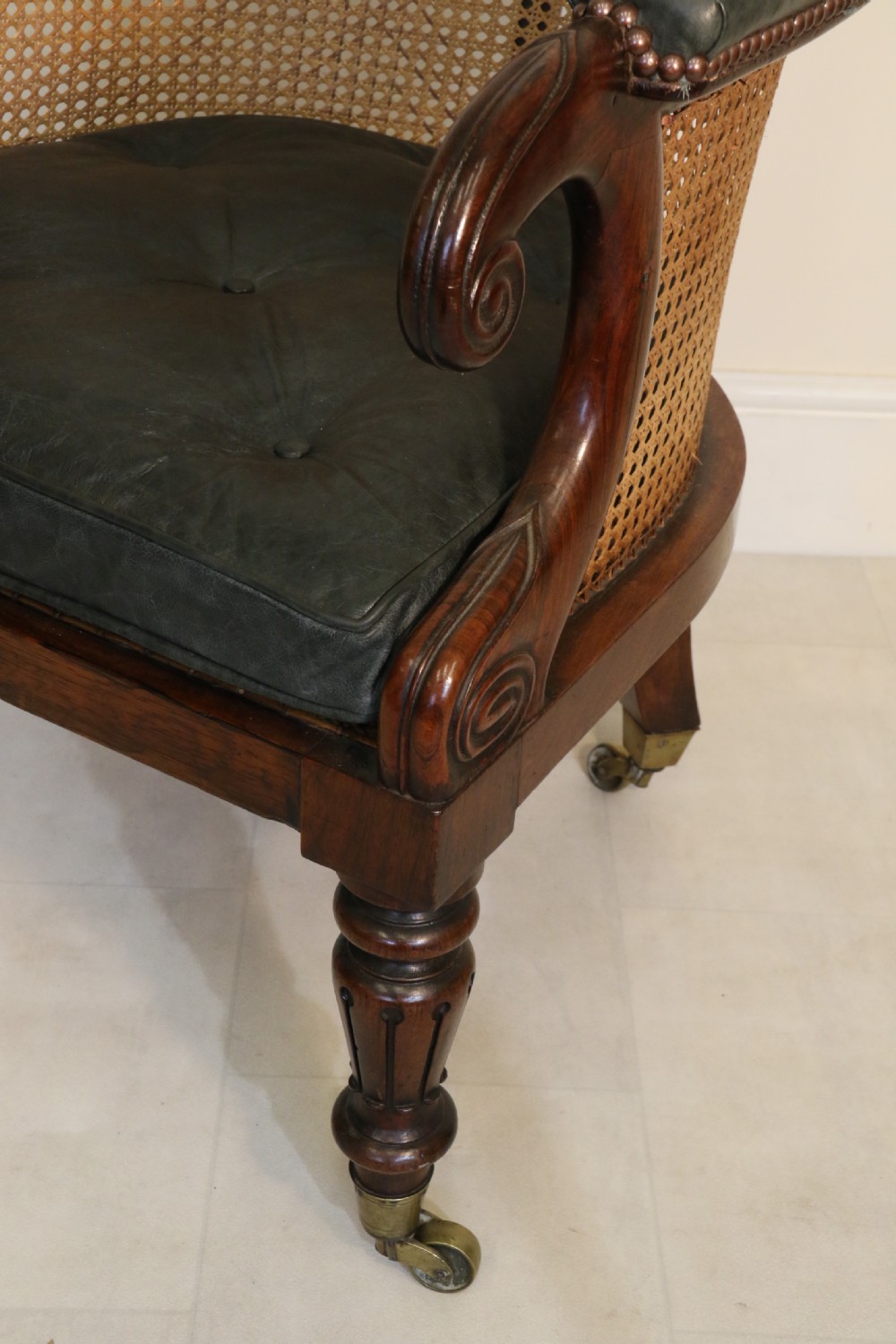 A pair of Regency rosewood bergere library armchairs with hand-woven cane panels, deep green leather cushions, scrolled arms, and turned legs on brass castors. View XV