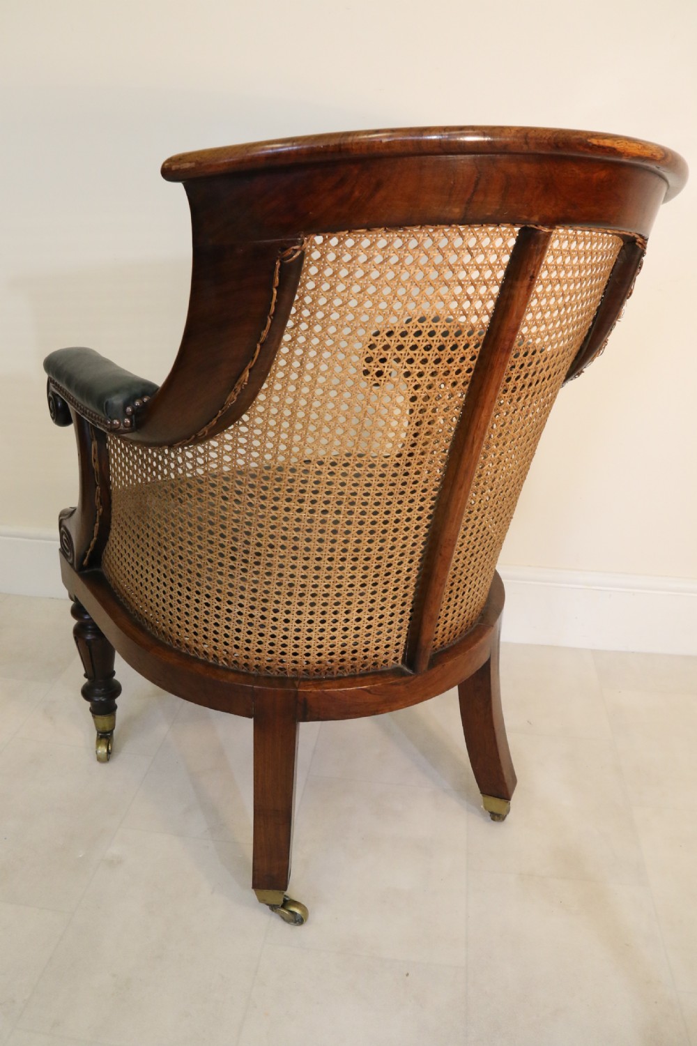 A pair of Regency rosewood bergere library armchairs with hand-woven cane panels, deep green leather cushions, scrolled arms, and turned legs on brass castors. View XVII