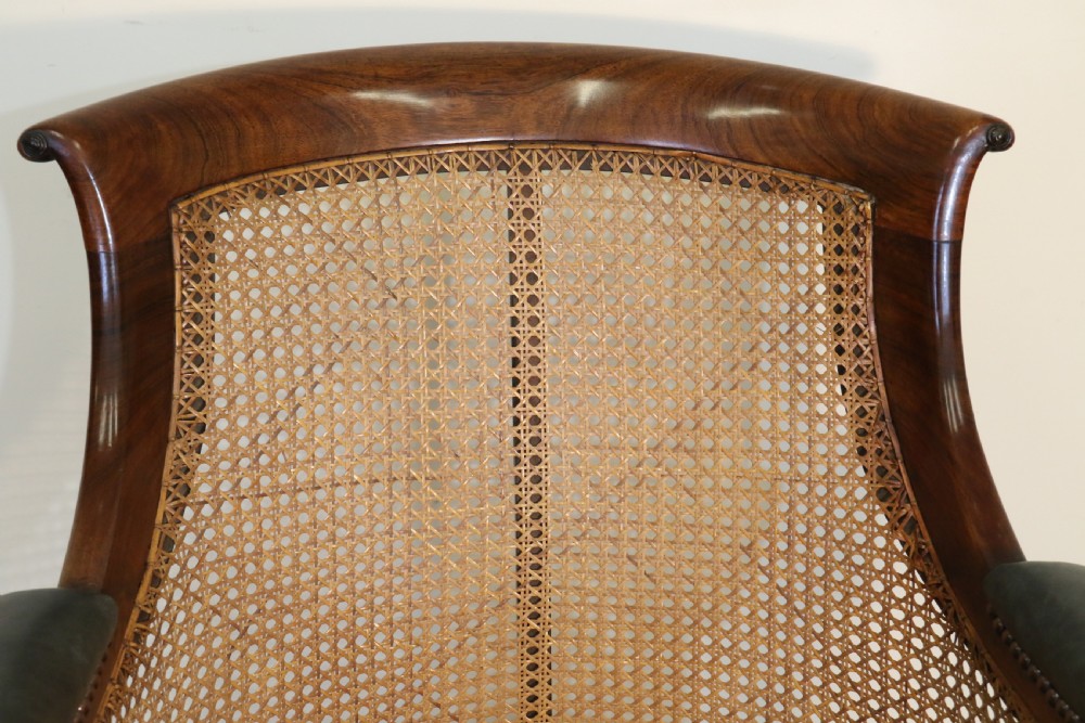 A pair of Regency rosewood bergere library armchairs with hand-woven cane panels, deep green leather cushions, scrolled arms, and turned legs on brass castors. View XIX