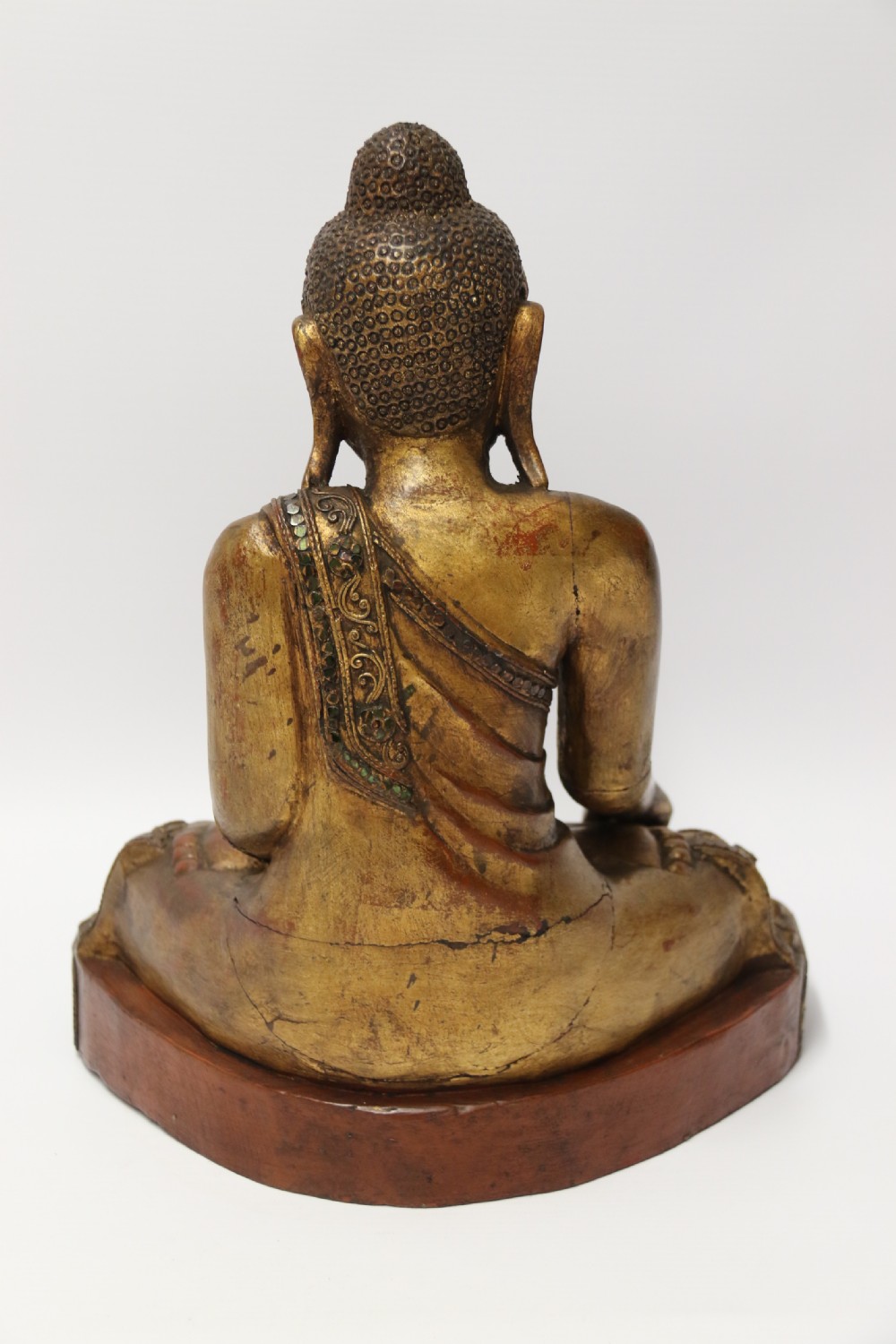 A carved wood Buddha figure in a seated posture decorated in gold gilding with ornamental glass inlay. View II