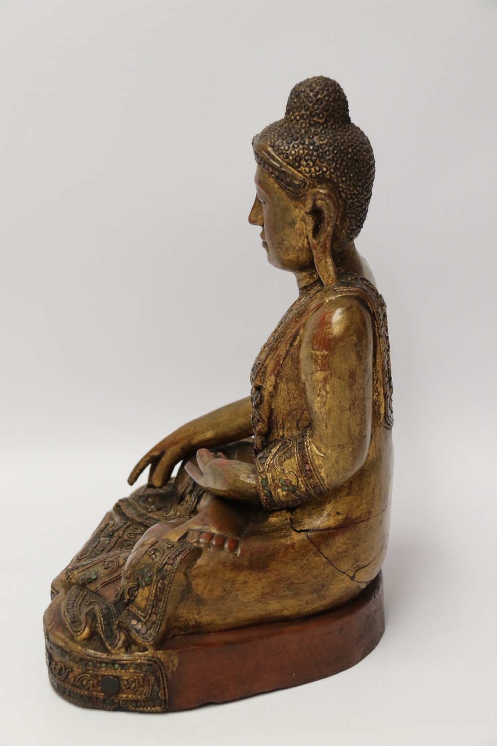 A carved wood Buddha figure in a seated posture decorated in gold gilding with ornamental glass inlay. View III