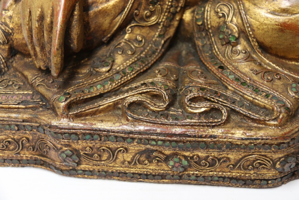 A carved wood Buddha figure in a seated posture decorated in gold gilding with ornamental glass inlay. View IV
