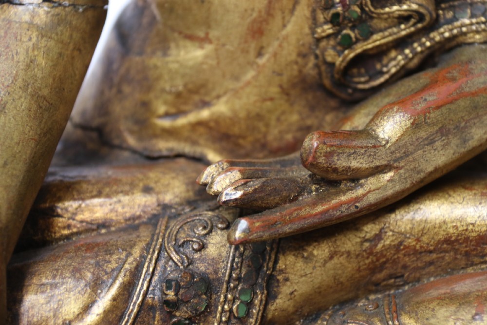 A carved wood Buddha figure in a seated posture decorated in gold gilding with ornamental glass inlay. View V