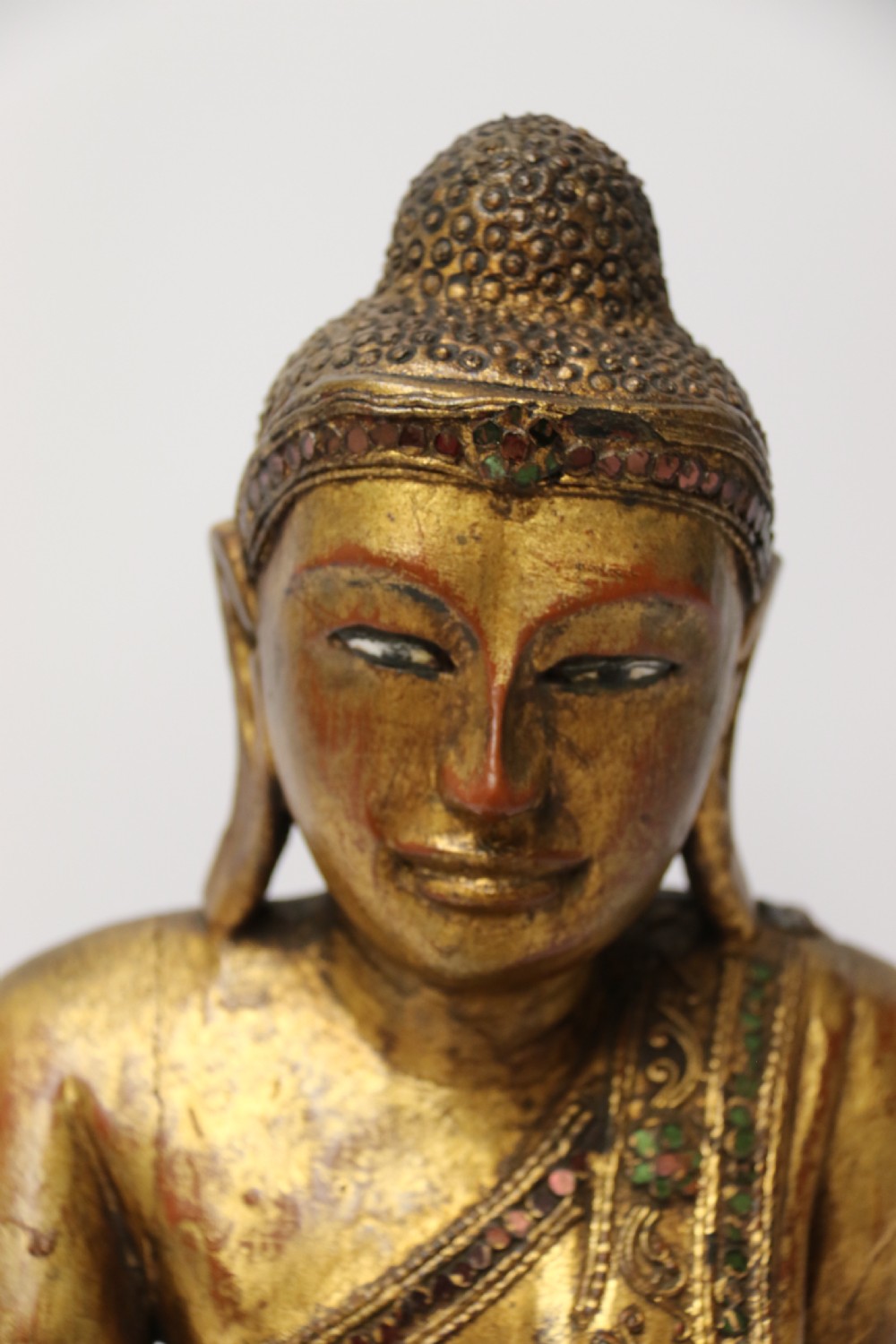 A carved wood Buddha figure in a seated posture decorated in gold gilding with ornamental glass inlay. View VI