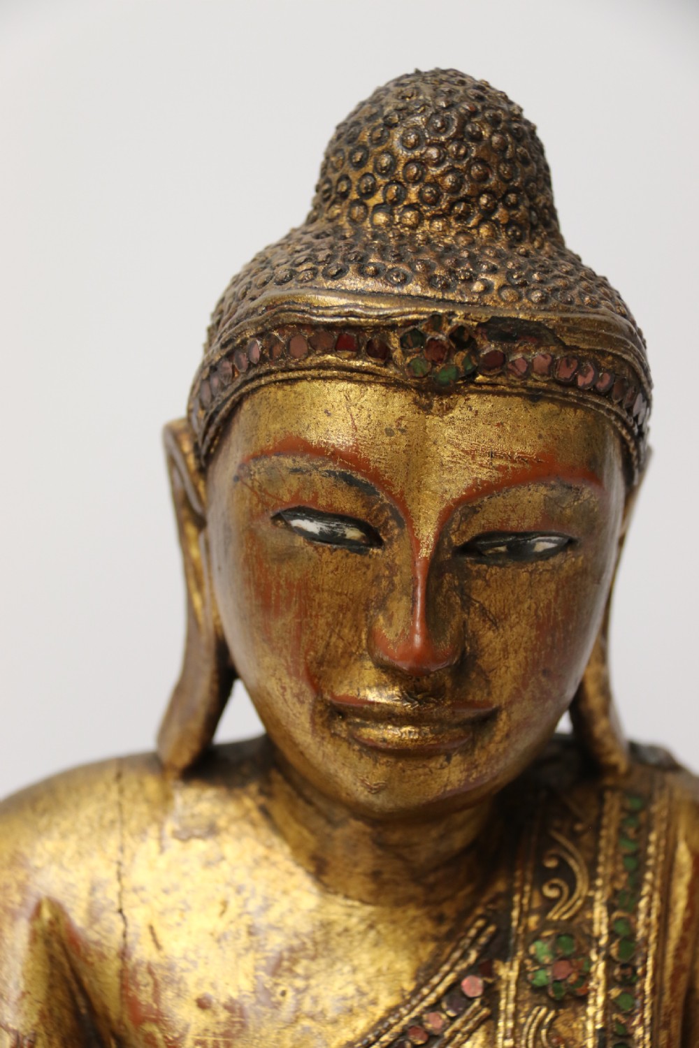A carved wood Buddha figure in a seated posture decorated in gold gilding with ornamental glass inlay. View VII