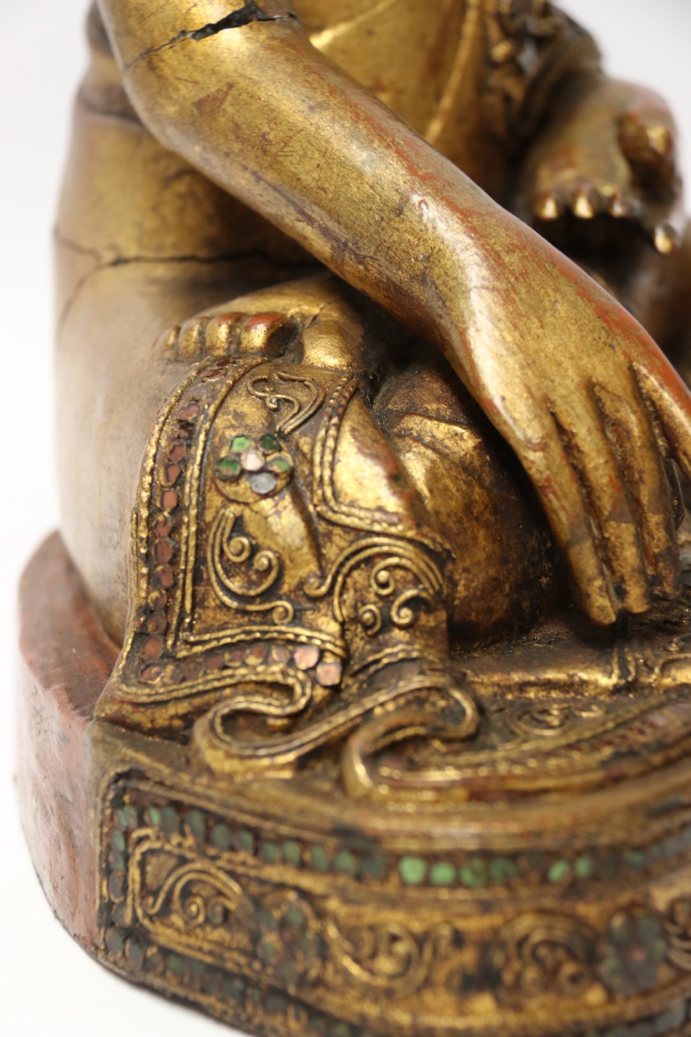 A carved wood Buddha figure in a seated posture decorated in gold gilding with ornamental glass inlay. View IX