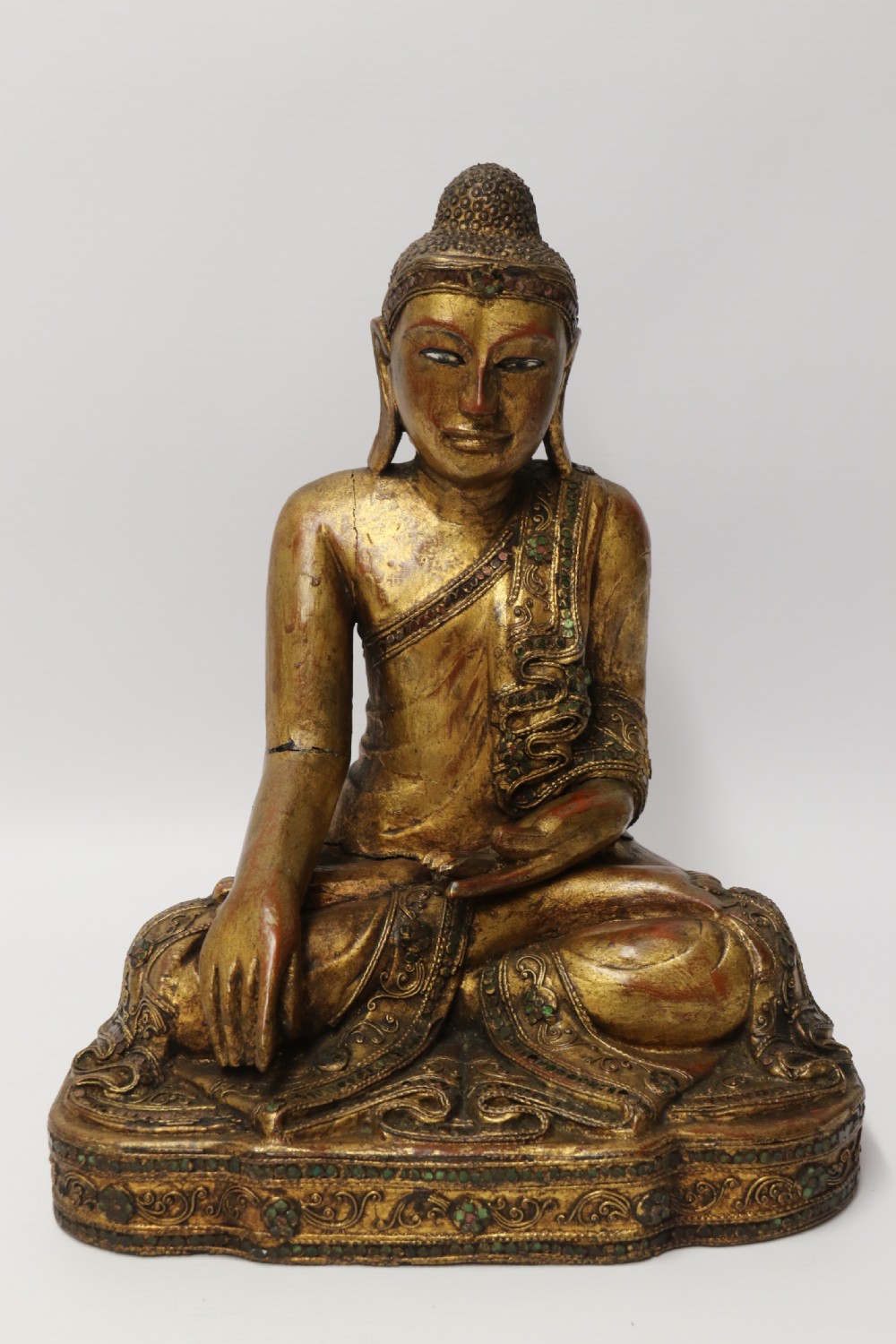 A carved wood Buddha figure in a seated posture decorated in gold gilding with ornamental glass inlay. View X