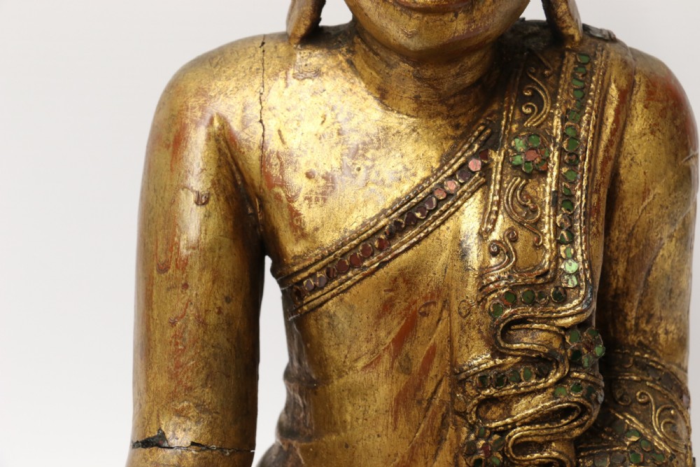 A carved wood Buddha figure in a seated posture decorated in gold gilding with ornamental glass inlay. View XI