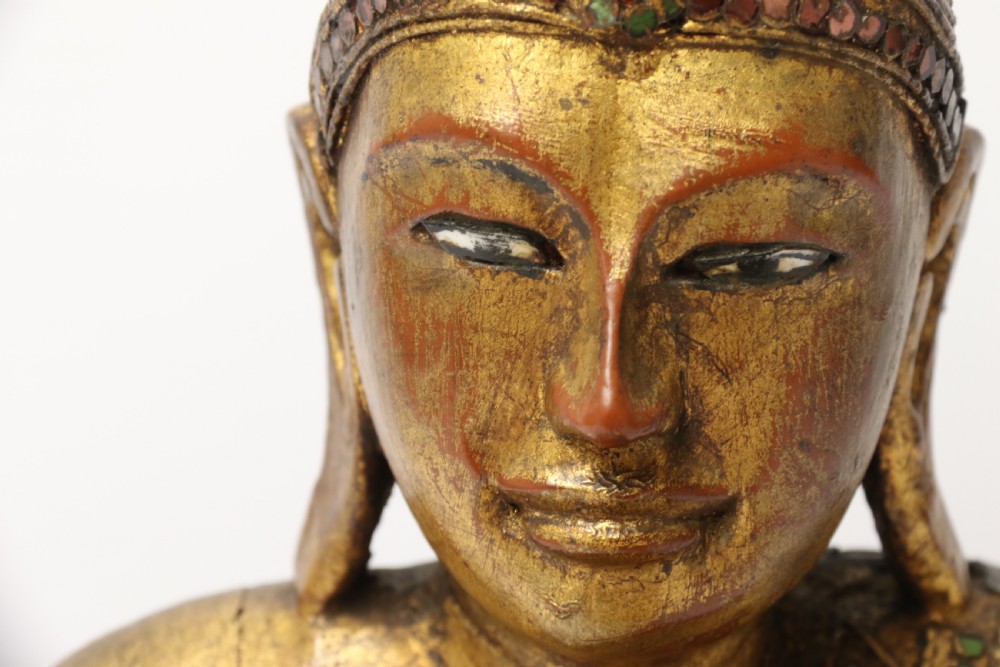 A carved wood Buddha figure in a seated posture decorated in gold gilding with ornamental glass inlay. View XII