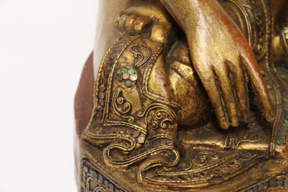 A carved wood Buddha figure in a seated posture decorated in gold gilding with ornamental glass inlay. View XIII