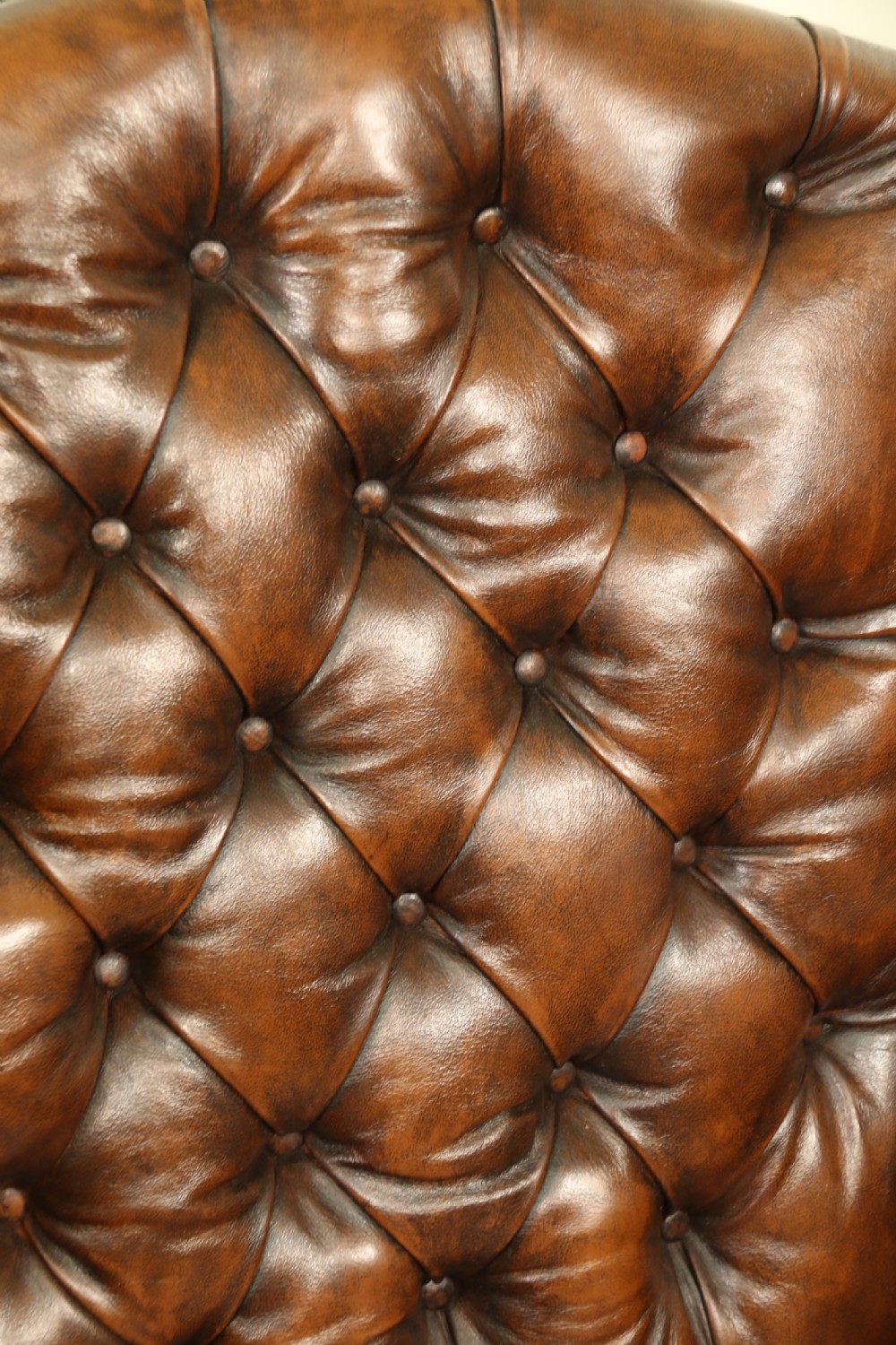 A George III chestnut brown leather wingback armchair featuring deep button tufting, brass stud detail, square wooden legs with stretchers, and brass castors. View XVI