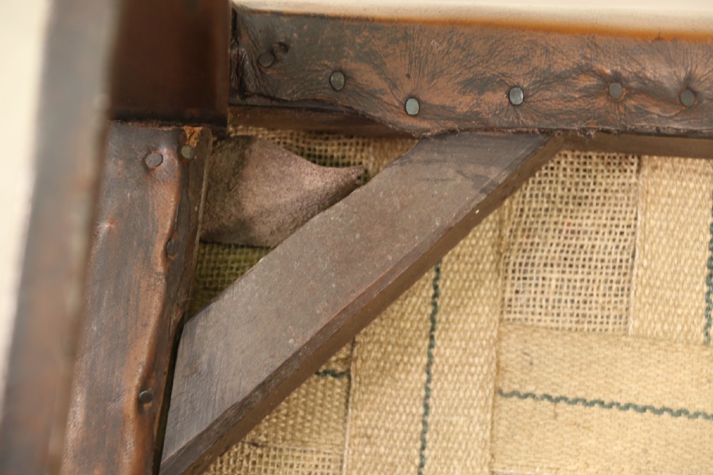 A George III chestnut brown leather wingback armchair featuring deep button tufting, brass stud detail, square wooden legs with stretchers, and brass castors. View XVIII