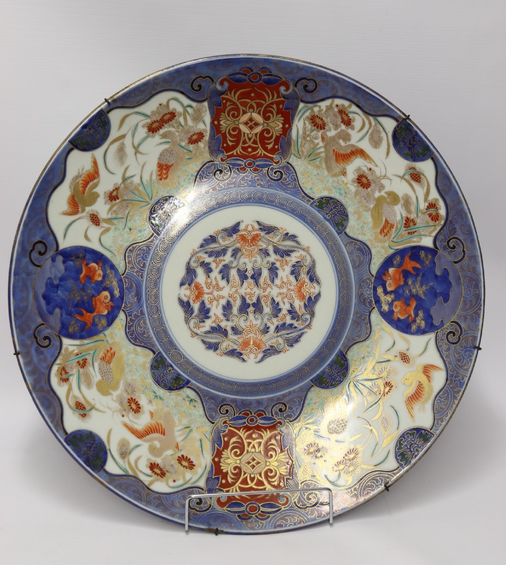 A circular hand-painted Japanese Imari porcelain charger featuring cobalt blue, iron red, and gilt decorative panels depicting birds, goldfish, and botanical motifs.