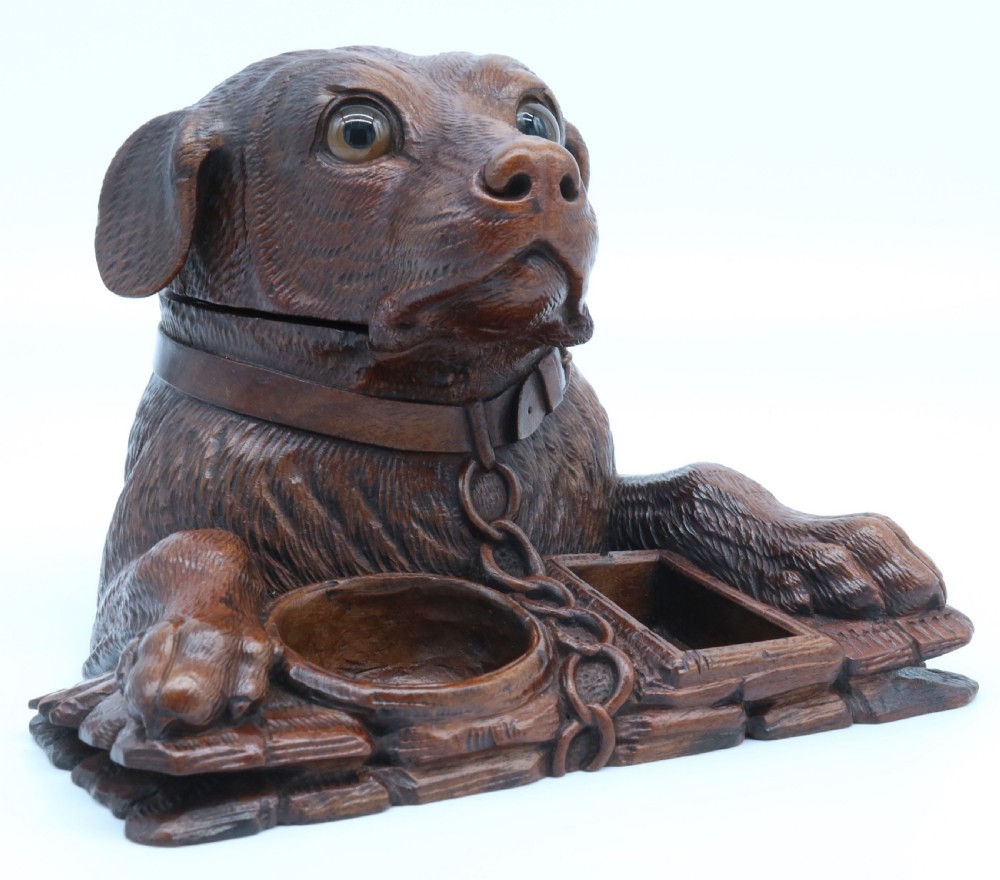 A 19th-century carved wooden tobacco box formed as a dog head with glass eyes and a hinged lid, set on a base with carved trays.