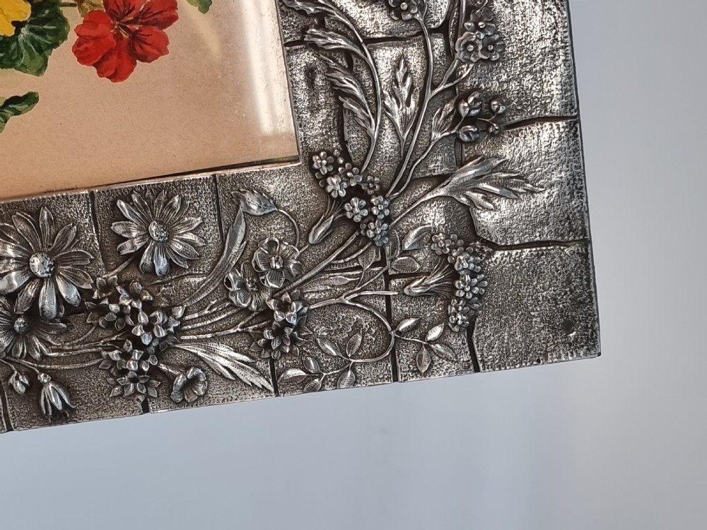An Aesthetic Movement pewter picture frame featuring embossed insect and floral relief decoration around a central floral watercolour illustration. View VIII