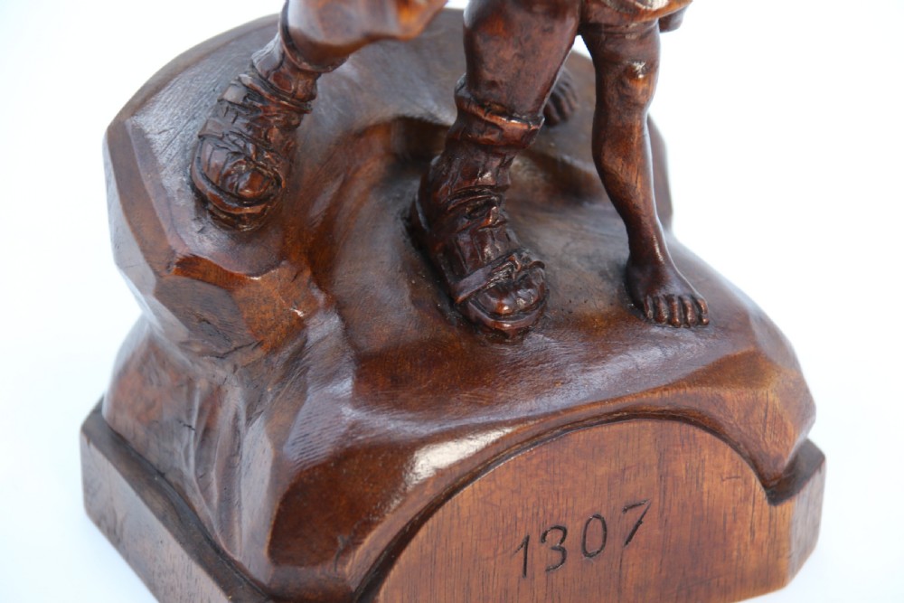 A hand-carved dark walnut wood sculpture depicting William Tell holding a crossbow alongside his son on a base carved with the date 1307. View XV
