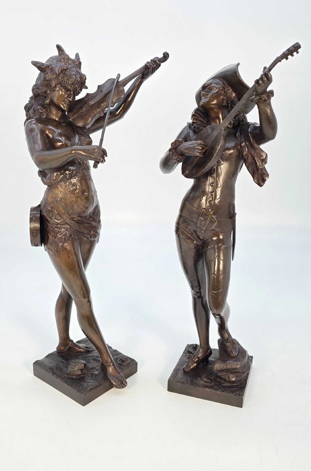 A pair of late 19th-century bronze statuettes depicting theatrical figures playing stringed musical instruments on square bases.