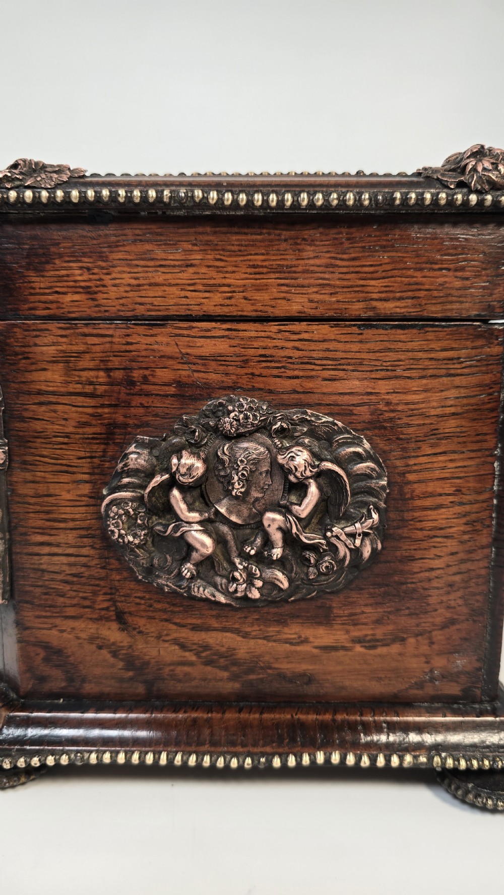 A dark carved oak tea caddy featuring copper relief caryatids, a central lock plate, and a decorative figural lid crest. View XI