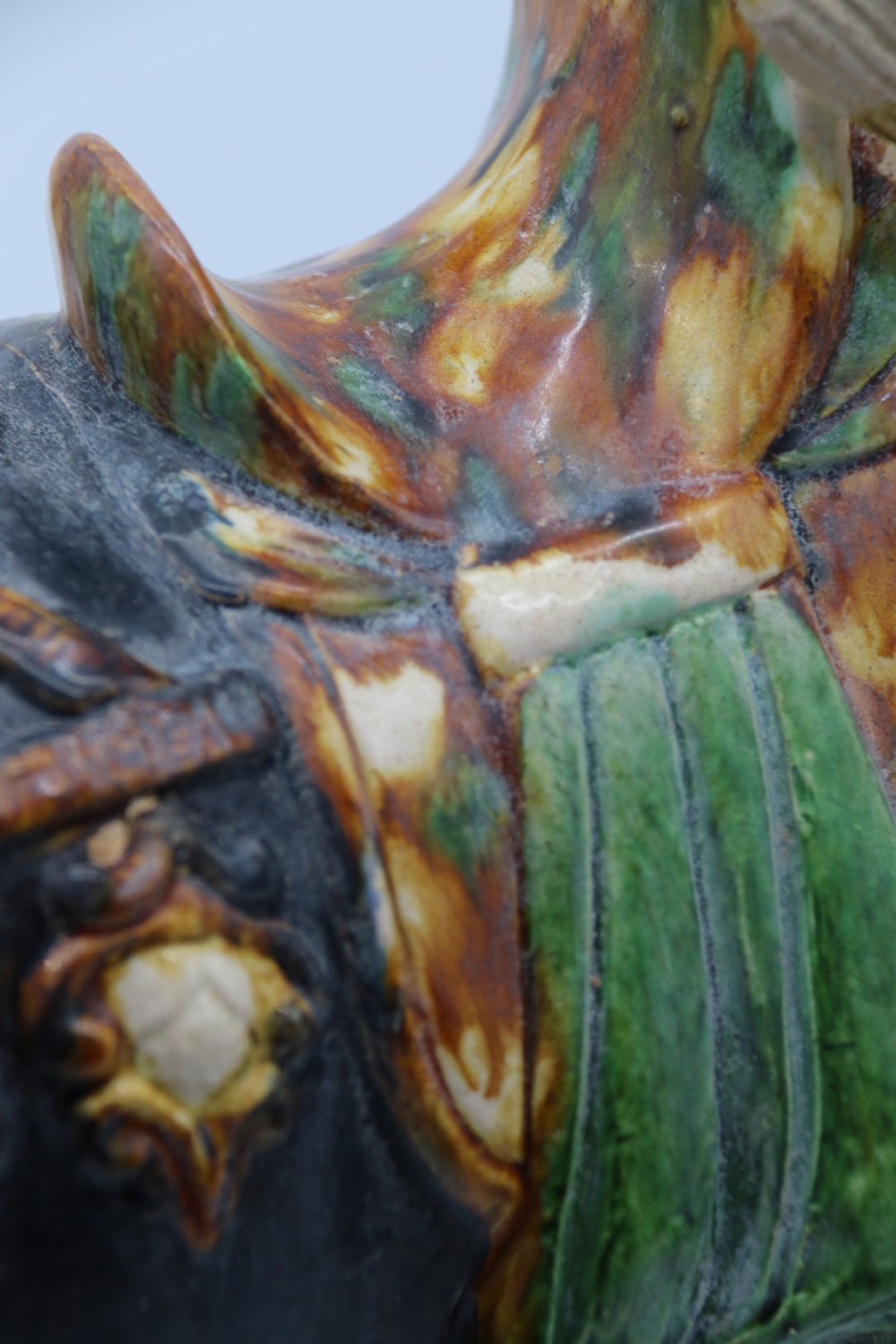 A ceramic Tang Dynasty style horse statue featuring a dark body glaze, amber mane, green draped saddle, and cream base. View XVI
