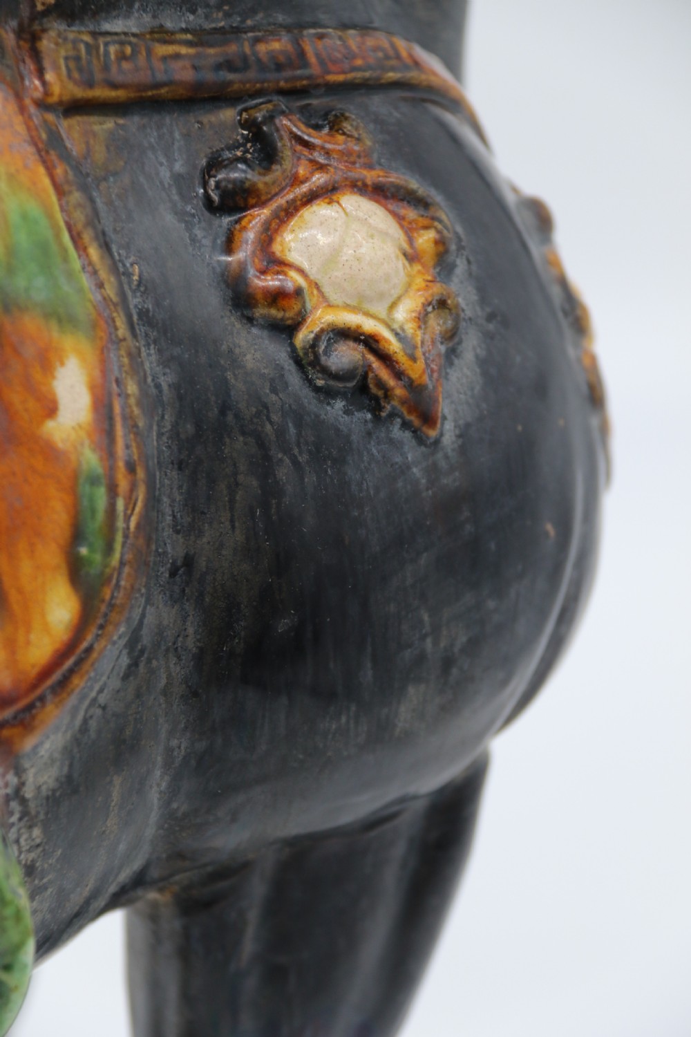 A ceramic Tang Dynasty style horse statue featuring a dark body glaze, amber mane, green draped saddle, and cream base. View XVII