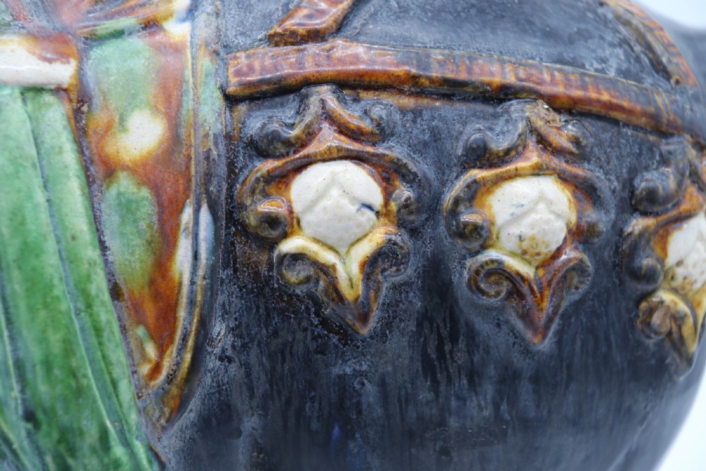 A ceramic Tang Dynasty style horse statue featuring a dark body glaze, amber mane, green draped saddle, and cream base. View XXI