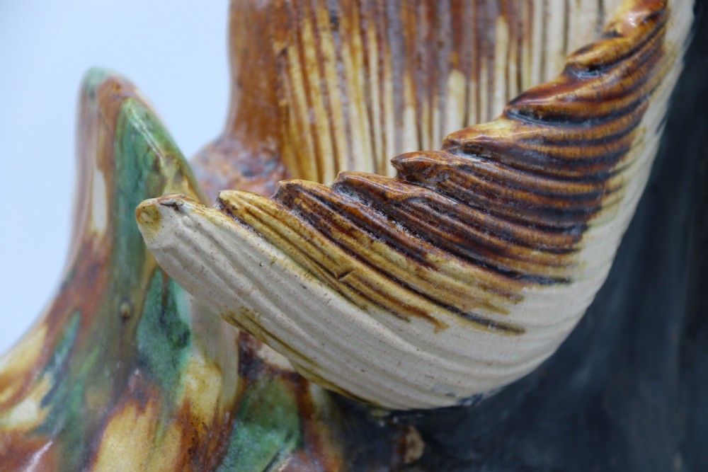 A ceramic Tang Dynasty style horse statue featuring a dark body glaze, amber mane, green draped saddle, and cream base. View XXIV