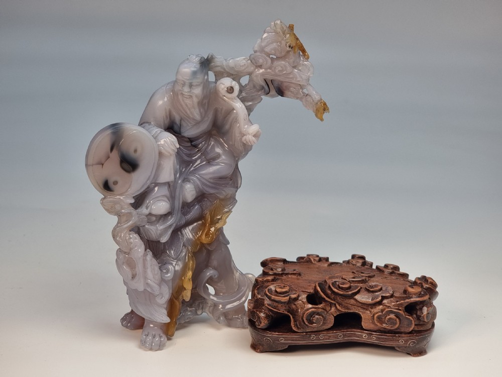 A hand-carved grey and honey-coloured agate figure group featuring a bearded Chinese figure resting on a fitted carved dark hardwood stand. View XVI