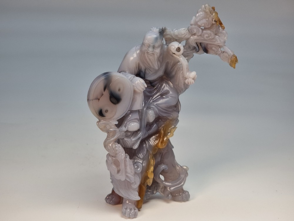 A hand-carved grey and honey-coloured agate figure group featuring a bearded Chinese figure resting on a fitted carved dark hardwood stand. View XVII
