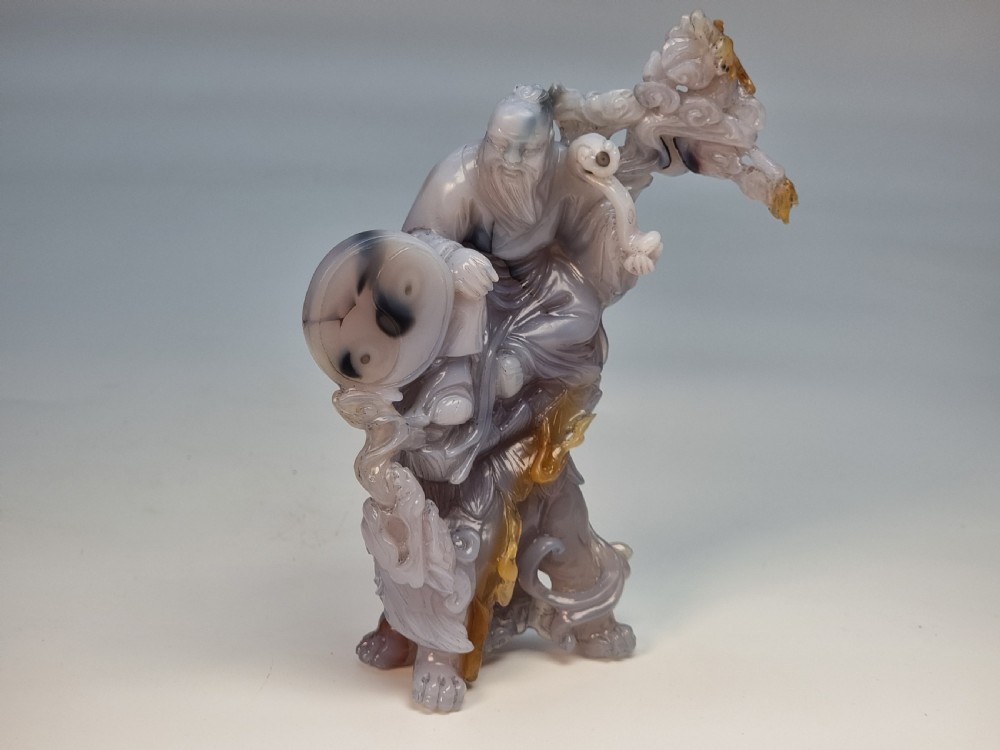 A hand-carved grey and honey-coloured agate figure group featuring a bearded Chinese figure resting on a fitted carved dark hardwood stand. View XVIII
