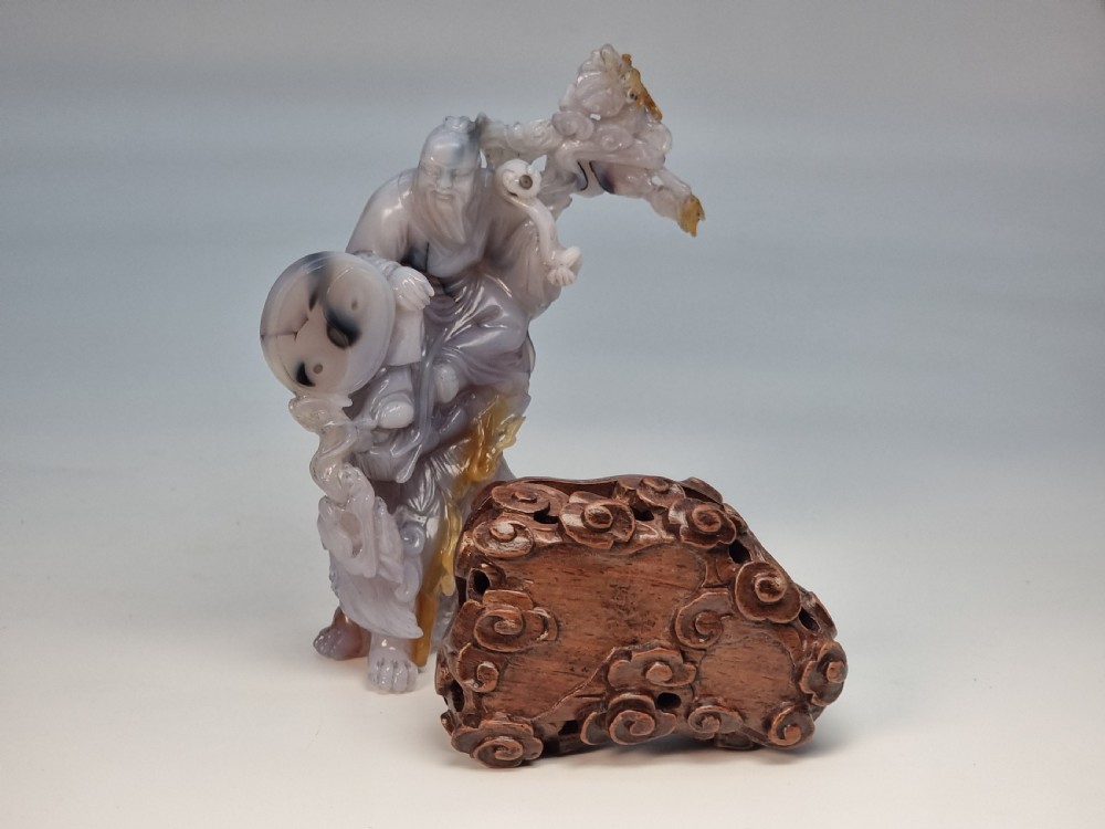 A hand-carved grey and honey-coloured agate figure group featuring a bearded Chinese figure resting on a fitted carved dark hardwood stand. View XIX