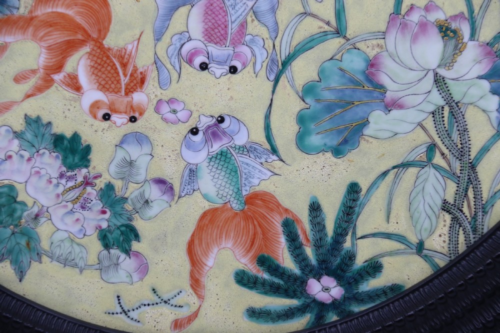 A circular framed Chinese porcelain plaque featuring vibrant hand-painted goldfish and lotus flowers on a yellow background enclosed in a carved dark frame. View III