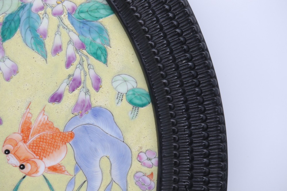 A circular framed Chinese porcelain plaque featuring vibrant hand-painted goldfish and lotus flowers on a yellow background enclosed in a carved dark frame. View IV