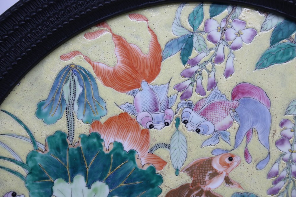 A circular framed Chinese porcelain plaque featuring vibrant hand-painted goldfish and lotus flowers on a yellow background enclosed in a carved dark frame. View V