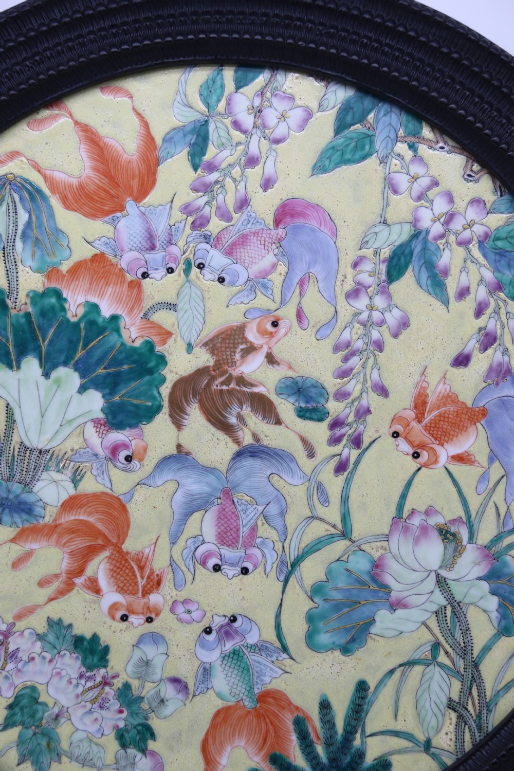 A circular framed Chinese porcelain plaque featuring vibrant hand-painted goldfish and lotus flowers on a yellow background enclosed in a carved dark frame. View VII