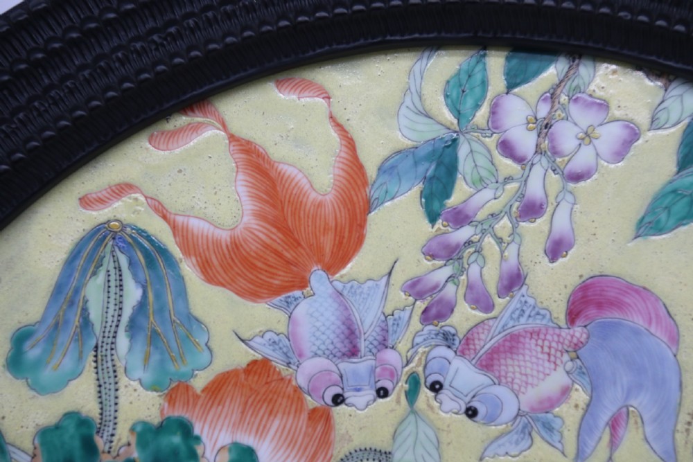 A circular framed Chinese porcelain plaque featuring vibrant hand-painted goldfish and lotus flowers on a yellow background enclosed in a carved dark frame. View VIII
