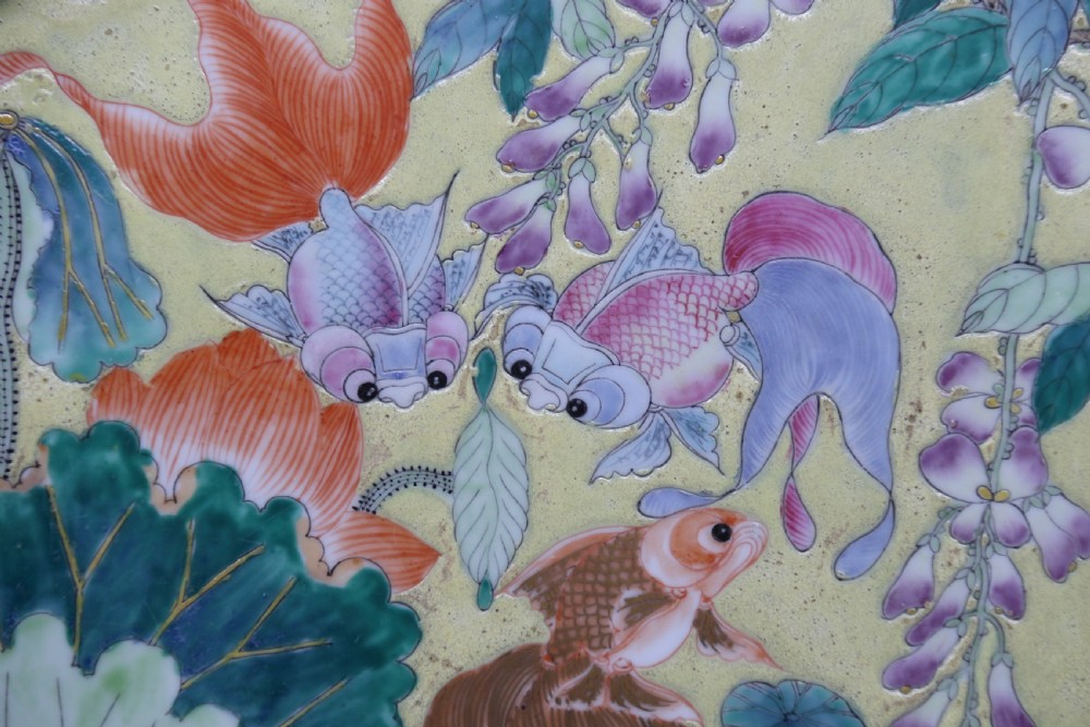 A circular framed Chinese porcelain plaque featuring vibrant hand-painted goldfish and lotus flowers on a yellow background enclosed in a carved dark frame. View IX