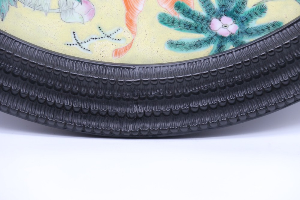 A circular framed Chinese porcelain plaque featuring vibrant hand-painted goldfish and lotus flowers on a yellow background enclosed in a carved dark frame. View X