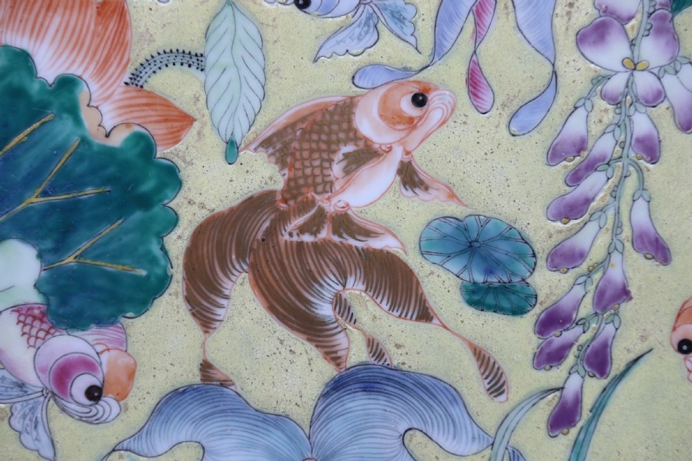 A circular framed Chinese porcelain plaque featuring vibrant hand-painted goldfish and lotus flowers on a yellow background enclosed in a carved dark frame. View XII