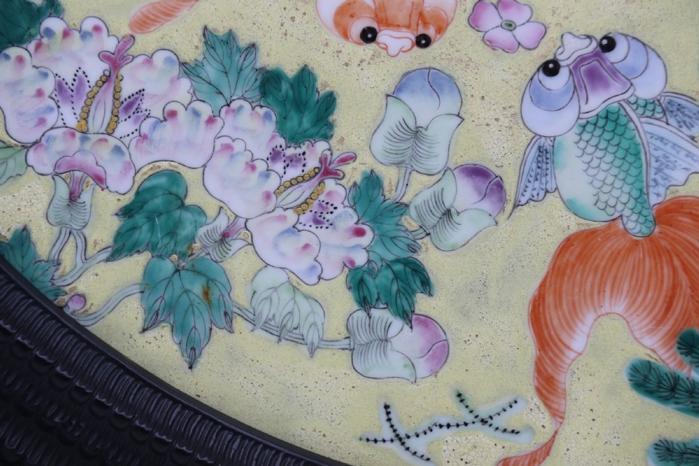 A circular framed Chinese porcelain plaque featuring vibrant hand-painted goldfish and lotus flowers on a yellow background enclosed in a carved dark frame. View XIV
