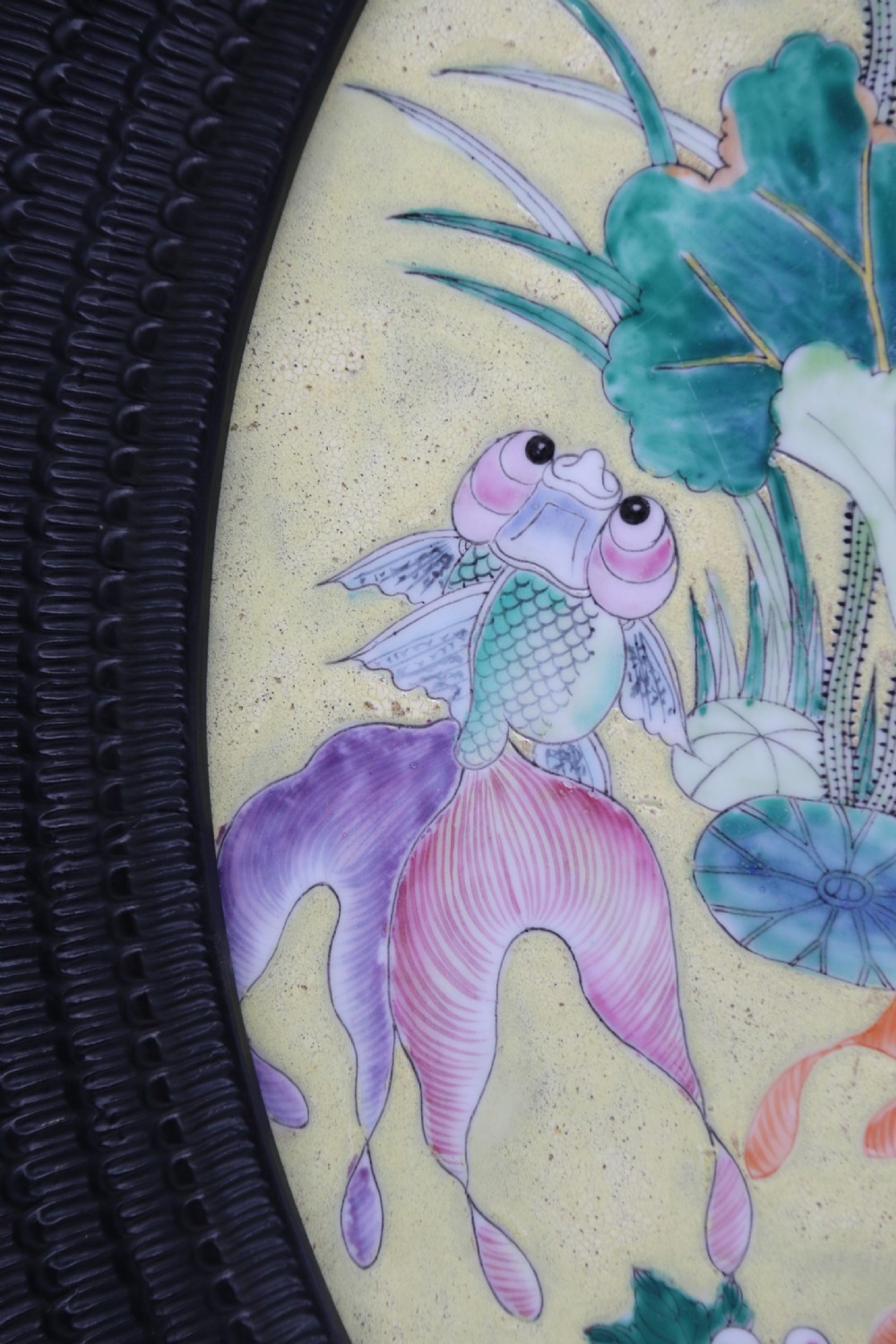 A circular framed Chinese porcelain plaque featuring vibrant hand-painted goldfish and lotus flowers on a yellow background enclosed in a carved dark frame. View XVI